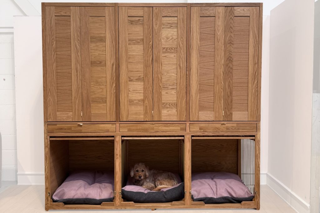Solid oak triple dog crate bootility dresser with three dog bedrooms, up and over doors, fitted cushions, three drawers and three tall cupboards above, with The Pet Carpenter's dog Finn resting in the centre bedroom